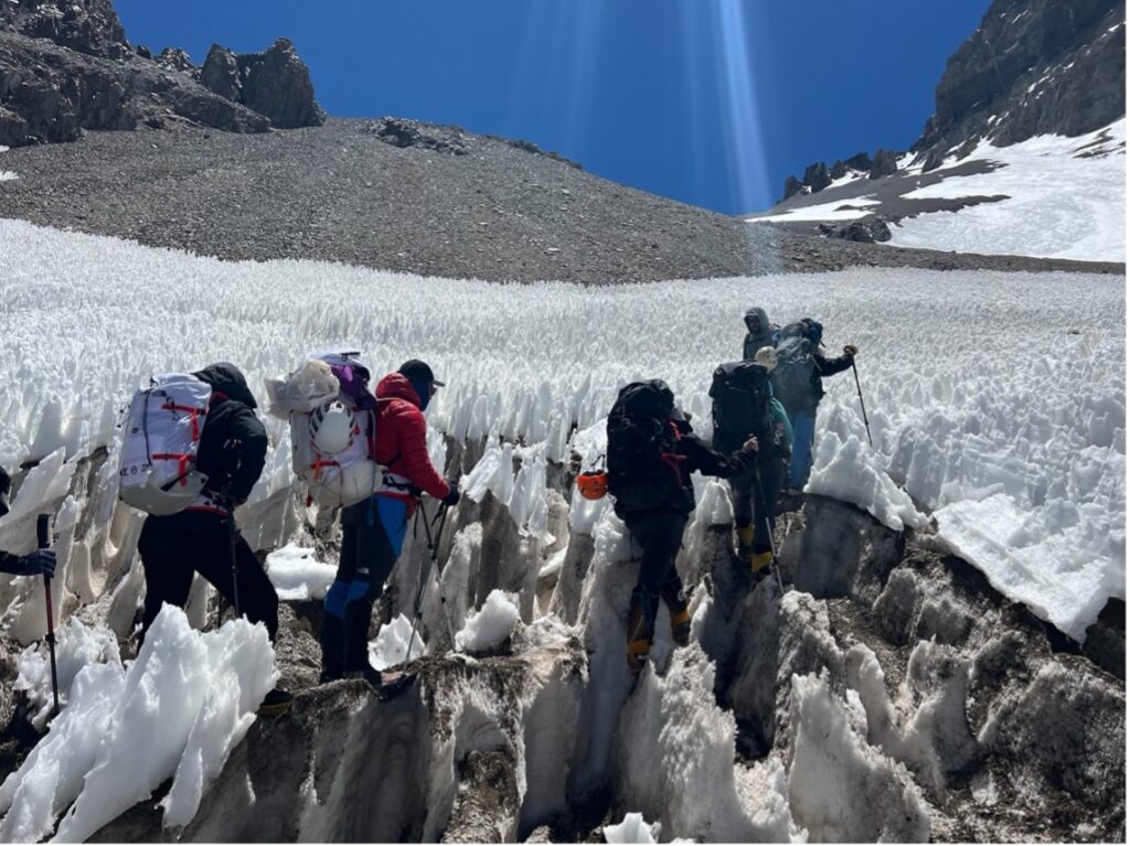 Climbers on Mount Aconcagua, dressed in cold weather gear and backpacks, navigating a penitentes snow field
