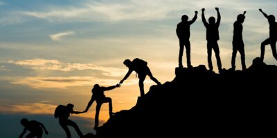 Group of people helping each other up a mountain