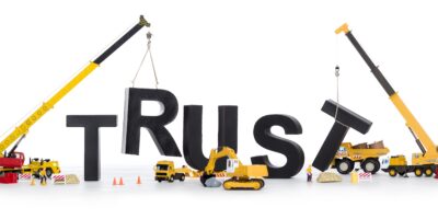 Two cranes and other construction equipment rebuilding the word "Trust"