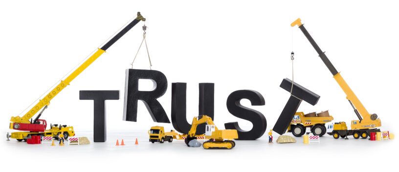 Two cranes and other construction equipment rebuilding the word "Trust"