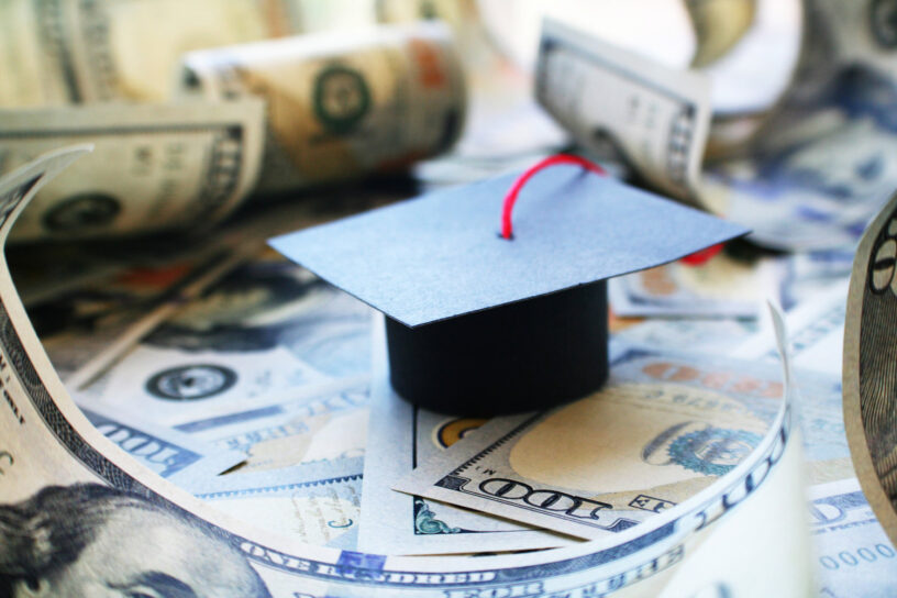 A graduation cap sitting on top of a pile of money